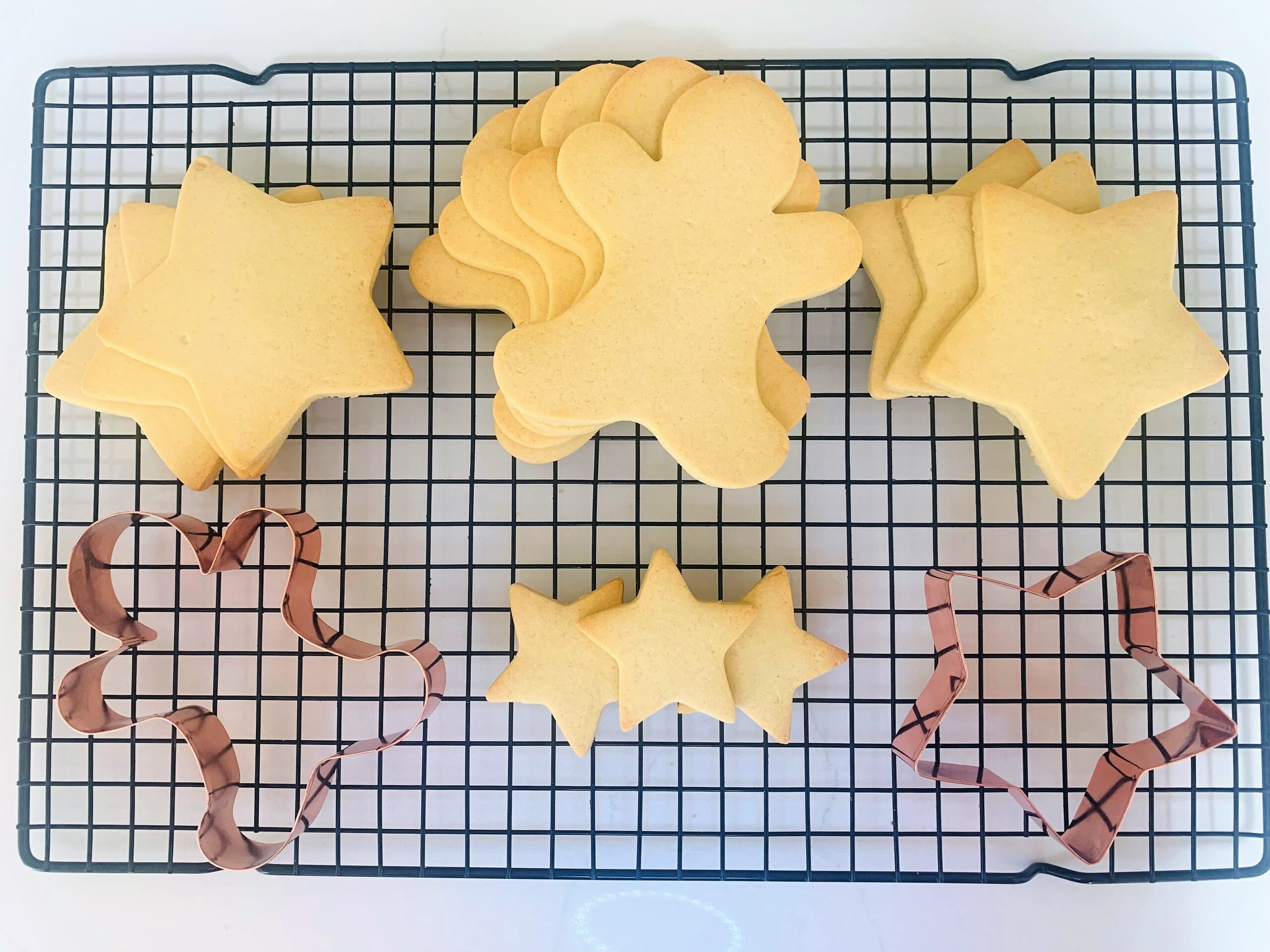 Picture of vanilla sugar cookies in the shapes of stars and gingerbread on a black wire rack with copper cookie cutters.